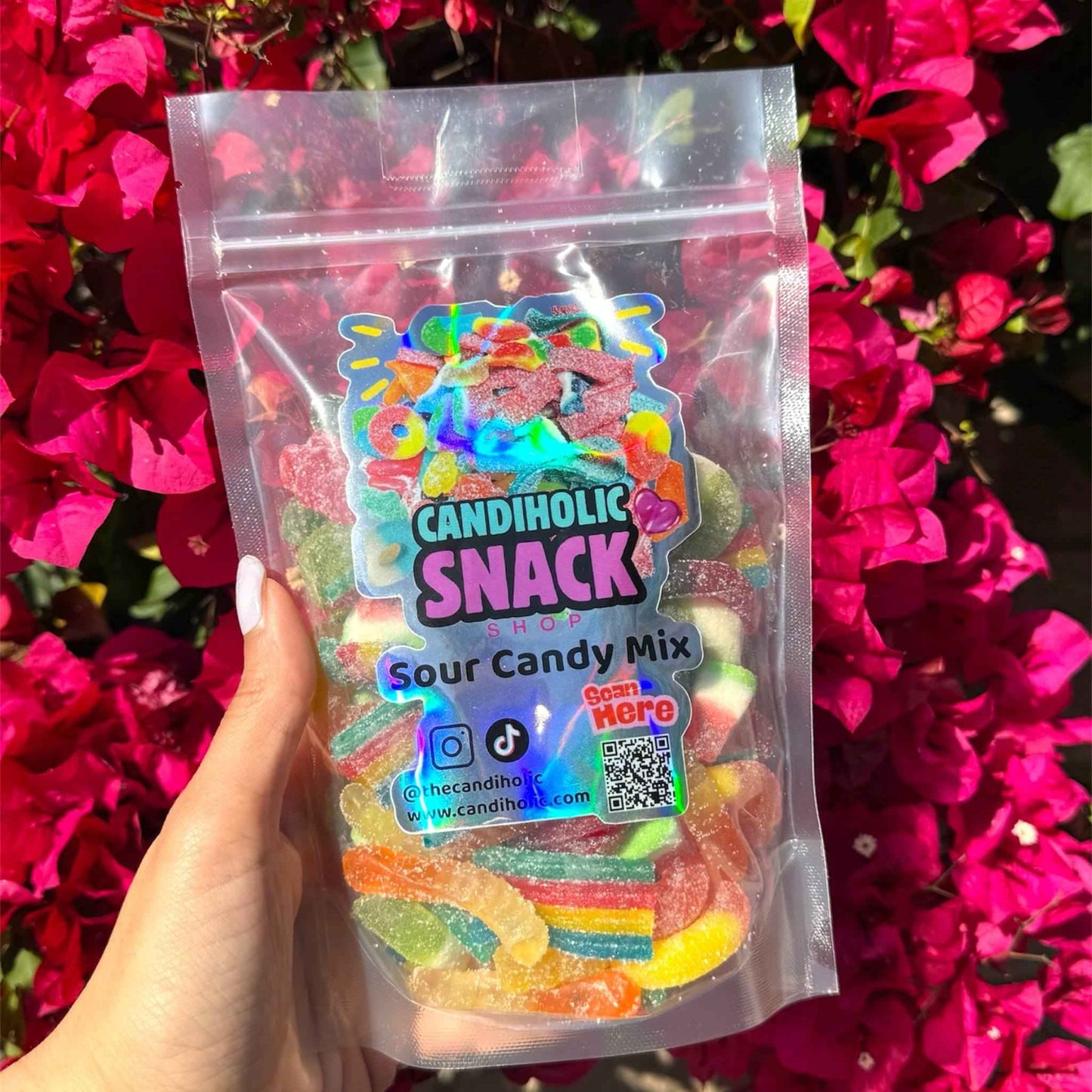 Hand holding two bags of assorted sour gummy candy mix with colorful candies inside