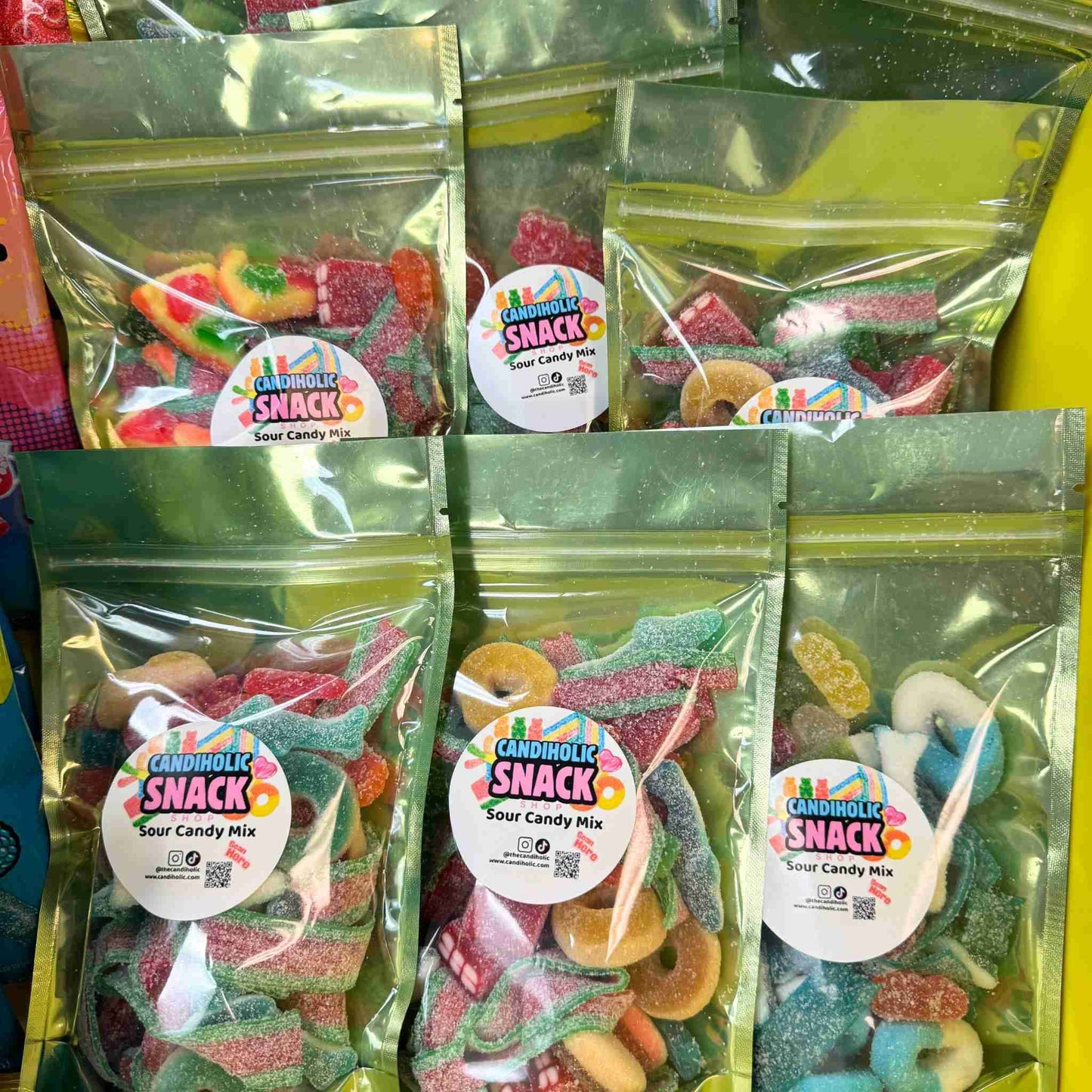 Display of packaged sour candy mix bags labeled Candiholic Snack Shop with colorful gummies inside